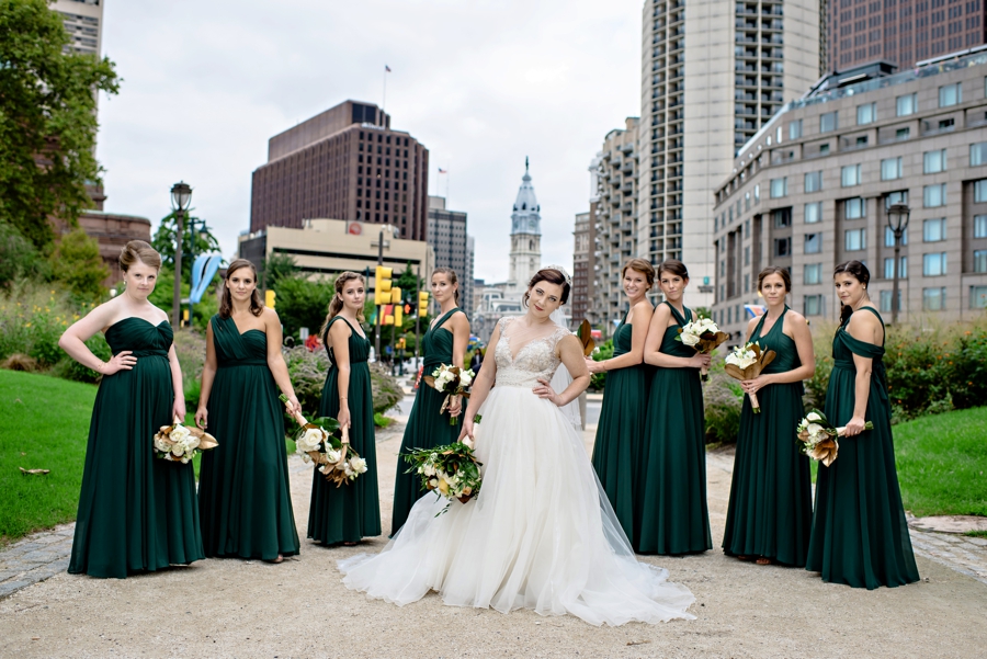 A bride and her bridesmaids pose with city hall behind them.